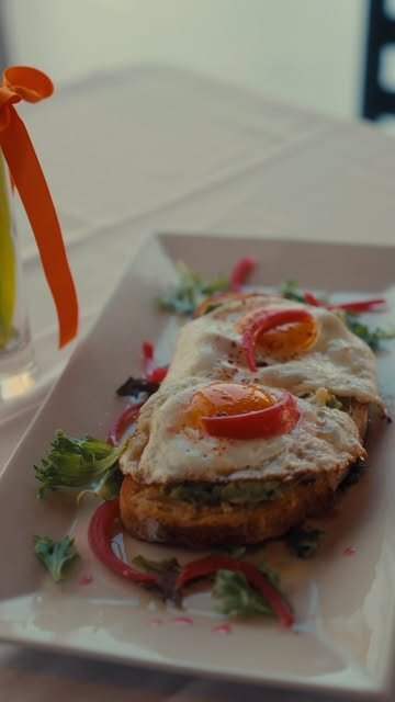 A plated Bai-Tee croque-madame — eggs over toasted sourdough with a fresh salad and a drink alongside